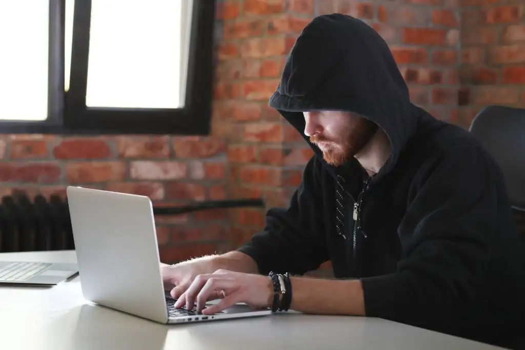 Een fraudeur in zwarte hoodie achter een laptop 